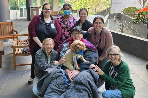5 West patient Richard and his family receive a visit from Lort Smith Pet Therapy dog Molly and her owner Sophie, in the ONJ Centre Wellness Garden. They are joined by nursing and admin staff from 5 West.